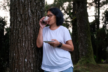 Asian woman leaning on a tree enjoying afternoon coffee in the park
