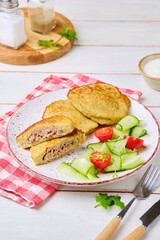 Potato pancakes stuffed with minced meat on a ceramic plate on a light wooden background. Served with fresh cucumber and cherry tomatoes. Belarusian cuisine.