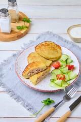 Potato pancakes stuffed with minced meat on a ceramic plate on a light wooden background. Served with fresh cucumber and cherry tomatoes. Belarusian cuisine.