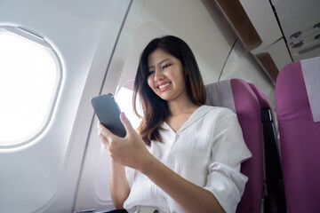 Asian businesswoman using smartphone on airplane seat during flight