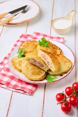 Potato pancakes stuffed with minced meat on a ceramic plate on a light wooden background. Served with sour cream. Belarusian cuisine.