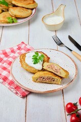 Potato pancakes stuffed with minced meat on a ceramic plate on a light wooden background. Served with sour cream. Belarusian cuisine.