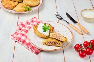 Potato pancakes stuffed with minced meat on a ceramic plate on a light wooden background. Served with sour cream. Belarusian cuisine.
