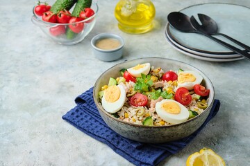French rice salad with canned tuna, cherry tomatoes, corn and cucumber in a ceramic bowl on a gray concrete background. Summer Picnic salad.