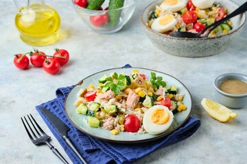 French rice salad with canned tuna, cherry tomatoes, corn and cucumber on a ceramic plate on a gray concrete background. Summer Picnic salad.