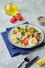 French rice salad with canned tuna, cherry tomatoes, corn and cucumber on a ceramic plate on a gray concrete background. Summer Picnic salad.