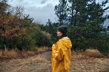 Young woman in yellow raincoat standing in field, contemplating distant journey in search of beauty and adventure