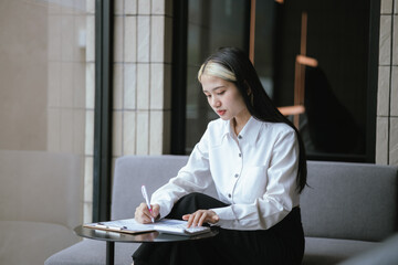 Modern Asian businesswoman sitting and working using a laptop Smart phone in office work