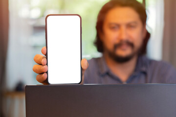 Adult Asian man holding and show a mobile phone with isolate screen in front of laptop computer.
