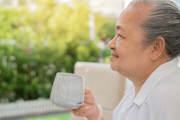 Side view portrait of senior Asian woman holding a cup of coffee in the garden at home.