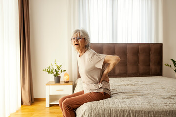 A senior woman is having backache and having troubles to get out from a bed in the morning.