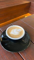 Black cup of cappuccino with latte art  on saucer on wooden background