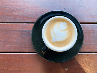 Black cup of cappuccino with latte art  on saucer on wooden background