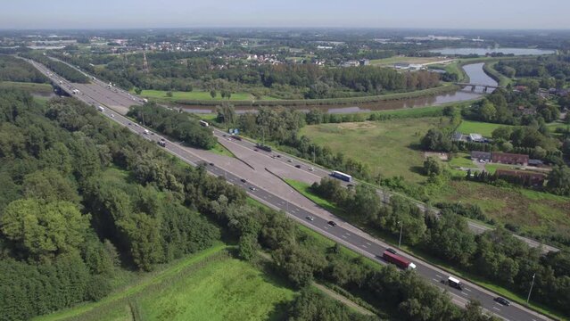 Expansive aerial panorama capturing the E19 highway between Brussels and Antwerp, viewed from Mechelen. The footage shows the busy multilane highway cutting through a verdant landscape with vehicles