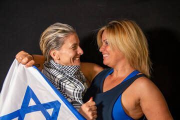 Two smiling women friendly interacting with each other wearing an Israeli flag and a Palestinian...
