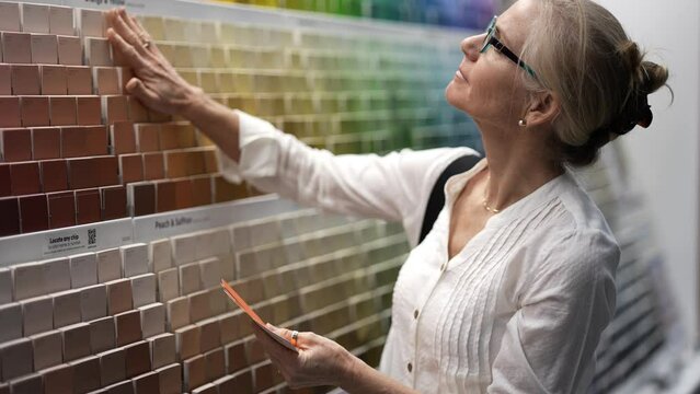 Closeup of smiling mature woman comparing color swatches at a paint display shopping for home redecorating renovation project, in a hardware store.