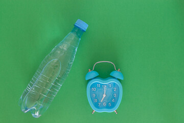 A water bottle and blue alarm clock on a green background. The concept of health. Water is good for...