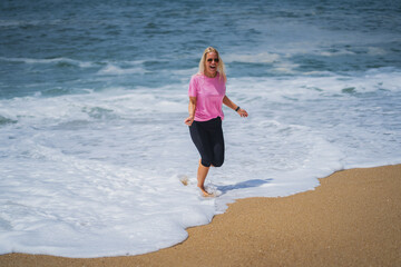 A young girl of European appearance in a pink T-shirt running on the Nazare beach during the waves...