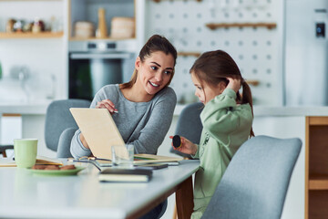 A loving mother helping her daughter study on a wooden laptop