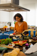 Attractive adult brunette woman in yellow dress cooking fresh vegetable salad in kitchen at home