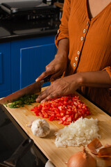 Close-up of a woman's hands, holding a knife, cutting vegetables on a cutting board in the kitchen