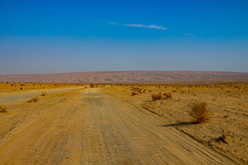 A country road through a sandy desert, barkhan belt, row of sand dunes on the horizon. Iran