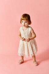 Little girl in white dress poses on pink background.