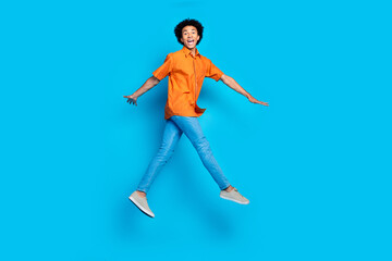 Full length photo of cheerful positive guy dressed orange shirt walking jumping high empty space...