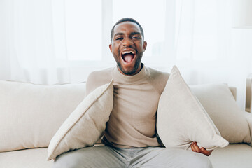 A Relaxed African American Man Sitting on a Modern Sofa in His Comfortable Living Room, Smiling and...