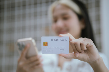 Attractive millennia Asian female holding her smartphone and credit card, using mobile banking app...