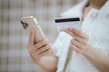 Attractive millennia Asian female holding her smartphone and credit card, using mobile banking app...