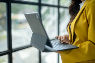 A woman wearing a yellow jacket is typing on a laptop