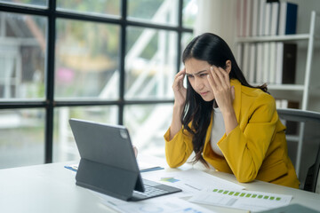 A woman in a yellow jacket is sitting at a desk with a laptop