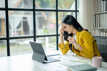 A woman in a yellow jacket is sitting at a desk with a laptop