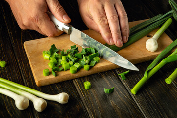 Cooking a flavorful vegetarian dish with garlic. The chef hands use a knife to cut young garlic on...