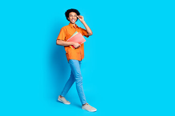 Full length photo of cheerful positive guy dressed orange shirt eyewear holding textbooks walking...