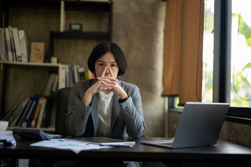 A woman sits at a desk with a laptop and a stack of papers