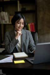 A woman is sitting at a desk with a laptop and a notebook