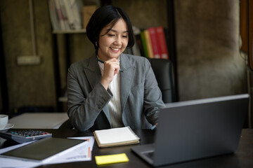 A woman is sitting at a desk with a laptop and a notebook