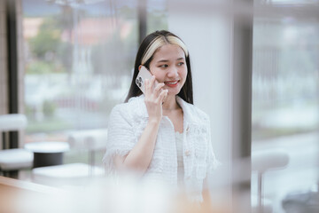 Fototapeta premium Smiling Asian woman standing and talking on the phone Businesswoman holding smartphone in office with copy space