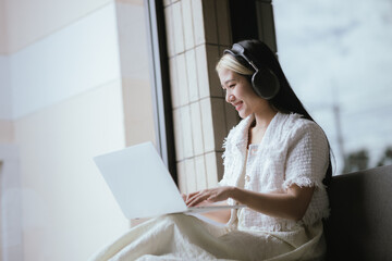Woman listening to music with headphones and using laptop or smart phone at home Relaxation holiday...