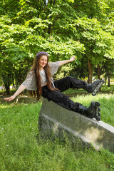 A teenage girl on roller skates sits on a granite block, arms outstretched and balancing, against...