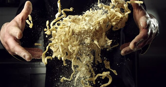 Super slow motion shots of artisan baker making homemade traditional recipe fresh raw italian pasta tagliatelle on rustic wooden table in bakery kitchen at 1000 fps.