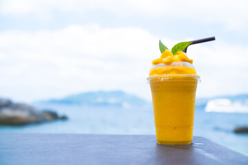 Smoothie made from fresh mango fruits against the backdrop of a seascape. Fruit and yoghurt ice cream decorated with leaves. Glass of tropical dessert close-up.