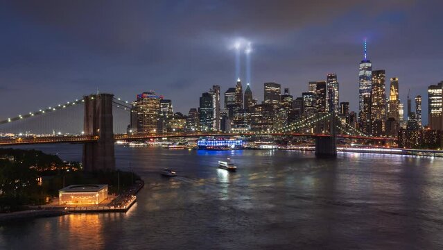 Ethereal twin beams of the September 11th Tribute in Light illuminating passing clouds in Lower Manhattan. Night view of Brooklyn Bridge, East River and financial district skyscrapers. New York City