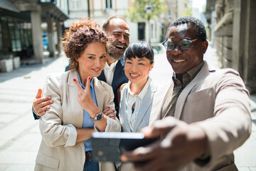 Group of diverse business people taking a selfie together on a sunny city street