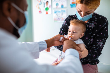 Pediatrician administering oral medication to an infant held by mother
