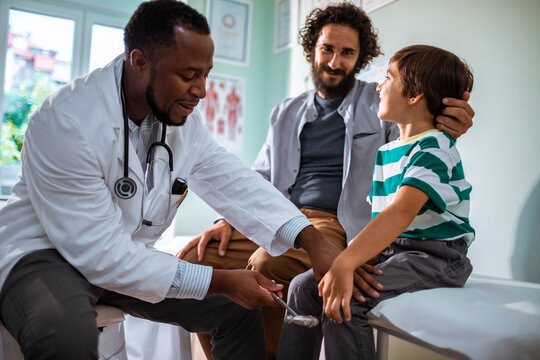 Pediatrician checking reflexes of a young boy in a medical clinic with his father present