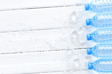 Plastic bottles with pure water and ice on white wooden backgrou