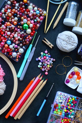 Colorful beads, coloring pencils, glitter, needles, string, hoop, tape and scissors on dark...